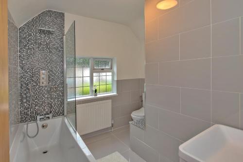 ein Bad mit einer Badewanne, einem Waschbecken und einem Fenster in der Unterkunft Finest Retreats - DeBarnes House in Solihull