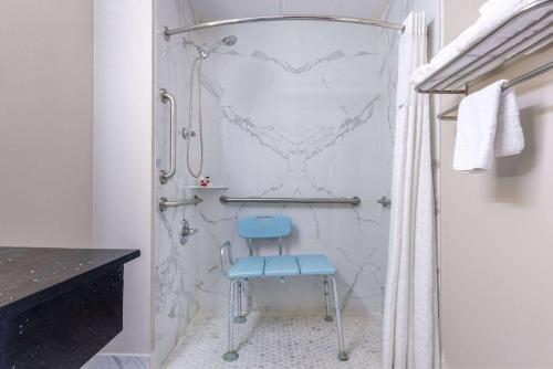 y baño con ducha y silla azul. en Days Inn & Suites by Wyndham Fort Bragg/Cross Creek Mall en Fayetteville