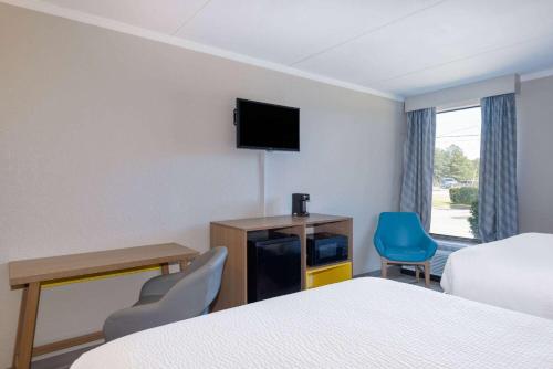 a hotel room with a bed and a desk and a tv at Days Inn & Suites by Wyndham Fort Bragg/Cross Creek Mall in Fayetteville