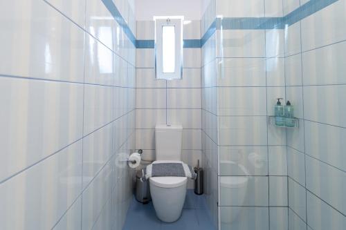 a white tiled bathroom with a toilet and a window at Joyful Guest Houses by 8essentially in Chania Town