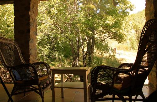 a porch with two chairs and a table and trees at Le Moulin de la Viorne, gîte avec piscine au cœur de la nature en Haute-Provence in Les Omergues
