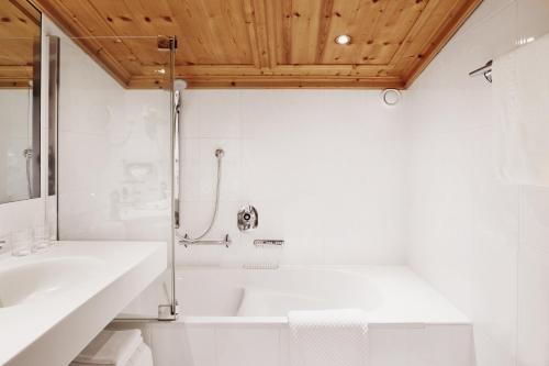 a white bathroom with a tub and a sink at Burg Hotel Oberlech in Lech am Arlberg