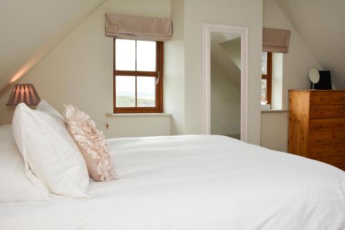 a white bed with white pillows and a window at Beautiful stone cottage with sea views in Sneem