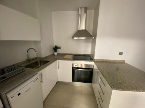 La cuisine est équipée de placards blancs, d'un évier et d'une cuisinière. dans l'établissement Apartaments Puigcardener 1, à Manresa