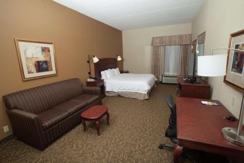 Hampton Inn Oneonta في أونيونتا: غرفه فندقيه بسرير واريكه