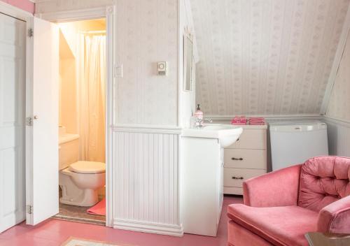 y baño con silla rosa, lavabo y aseo. en Bed & café Petit Papillon, en Grandes-Bergeronnes