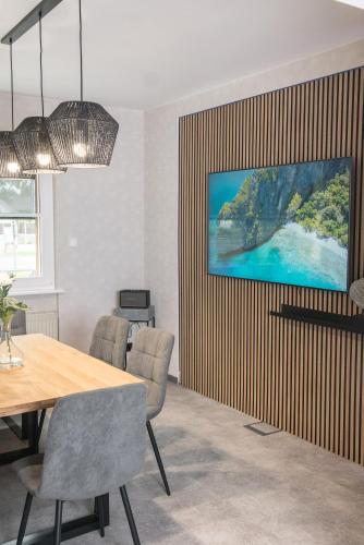 a dining room with a table and a tv on a wall at Triumph Ferienhäuser & Apartments in Rangsdorf