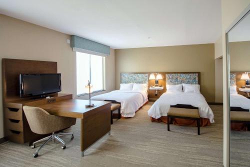 ポート・アーサーにあるHampton Inn & Suites Port Arthurのベッド2台、デスク、テレビが備わるホテルルームです。