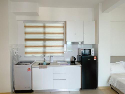 a kitchen with a black refrigerator and white cabinets at Mutiara Melaka Beach Resort by Minso in Tangga Batu