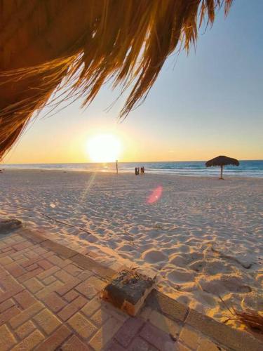 a sunset on a beach with an umbrella at North coast rent Chalet / شاليه للايجار في الساحل in Dawwār Abū Duray‘ah ‘Abd al Karīm