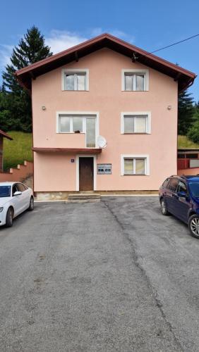 a pink house with two cars parked in a parking lot at Apartmani Klačar in Gornje Pale