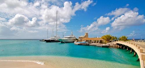 a dock with boats in the water next to a beach at Spinnaker, #127 Port St. Charles Marina, Speightstown - Waterfront Luxury in Saint Peter