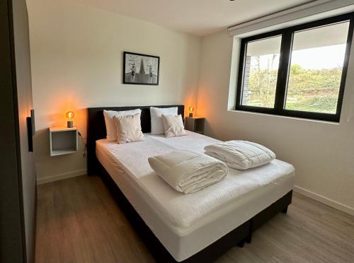 a bedroom with a bed with two pillows and a window at Design Apartment with 60m² terrace - heated inside pool and wellness facilities - very close to the beach in Cadzand