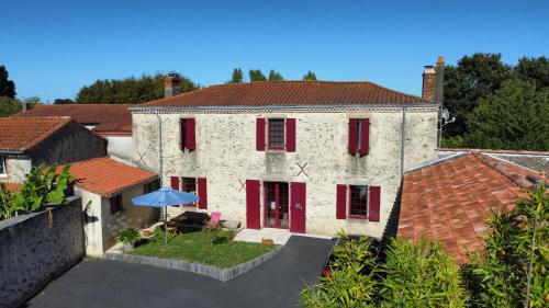 - un grand bâtiment blanc avec des fenêtres à volets rouges et un parasol dans l'établissement LA CHARMILLE Gîte et Chambre d'hôtes, à La Copechagnière