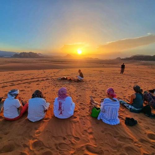 a group of people sitting on the beach watching the sunset at golden day in Wadi Rum
