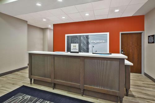 an office lobby with an orange accent wall at Hampton Inn by Hilton Detroit Dearborn, MI in Dearborn