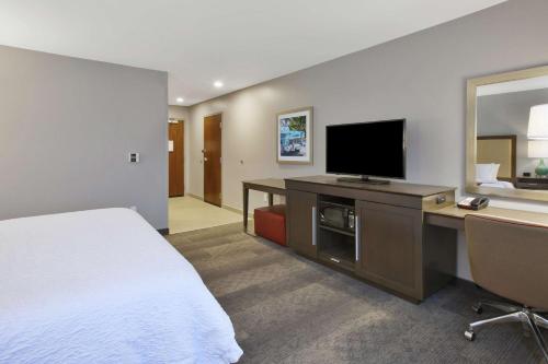 a hotel room with a bed and a desk with a television at Hampton Inn by Hilton Detroit Dearborn, MI in Dearborn