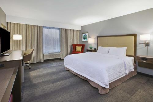 Hampton Inn by Hilton Detroit Dearborn, MI في ديربورن: غرفة فندقية بسرير وتلفزيون بشاشة مسطحة