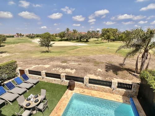 einen Blick über einen Pool mit Stühlen und einen Golfplatz in der Unterkunft Luxurious Frontline Golf Villa on Mar Menor Golf in Torre-Pacheco