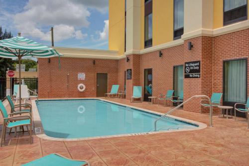 a swimming pool in front of a building with chairs and an umbrella at Hampton Inn & Suites by Hilton Tampa Busch Gardens Area in Tampa