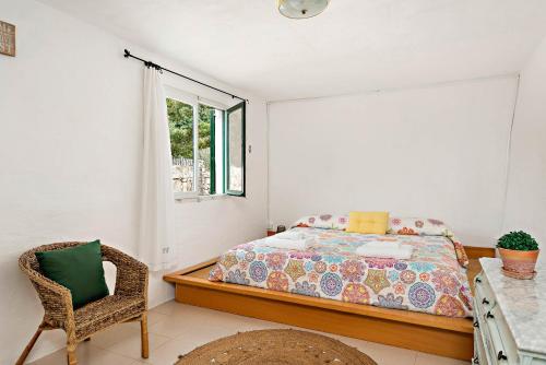 a bedroom with a bed and a chair and a window at Casita Estancia d'en Carretero- Biniarroca in Es Castell