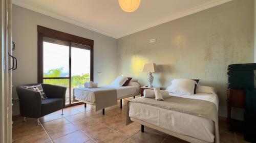 een slaapkamer met 2 bedden, een stoel en een raam bij Villa Huerta del Sur - Piscina privada y barbacoa in Alhaurín el Grande