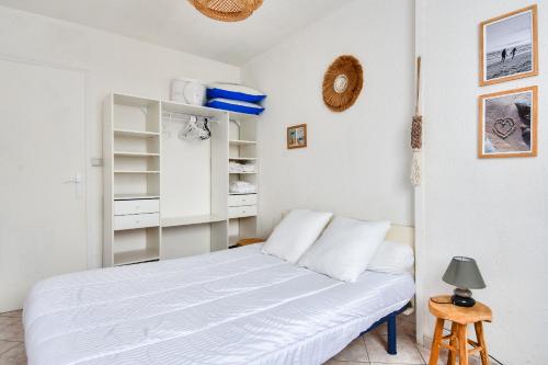 Cette petite chambre comprend un lit blanc et un tabouret. dans l'établissement 100m de la plage des Mouettes, appartement pour 4, à Saint-Hilaire-de-Riez