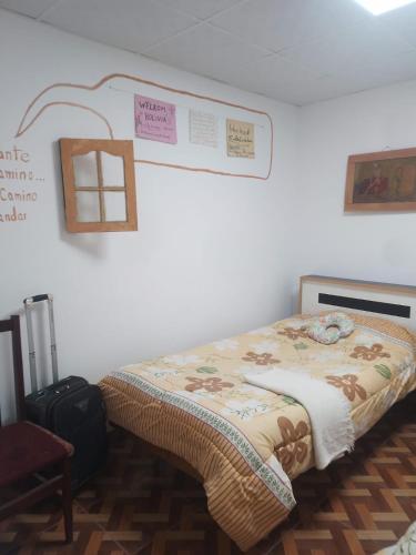 a room with a bed with a blanket and a suitcase at Hostal Casa Grande in Villazón