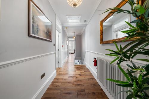 a hallway with white walls and wood floors and a mirror at Royal Greenwich Hospitality in London