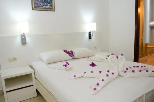 ein weißes Bett mit weißen Socken und lila Blumen darauf in der Unterkunft Bodrum Park Hotel in Gümbet