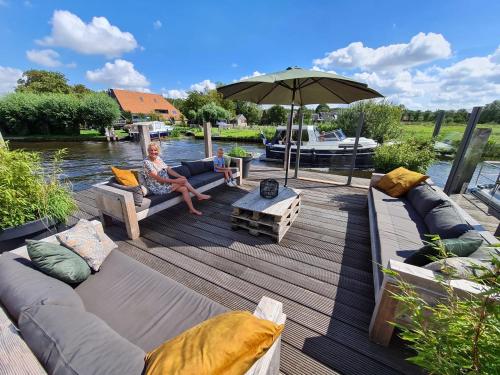 une femme assise sur une terrasse en bois avec un parasol dans l'établissement Verblijf bij Bynt, à Sneek