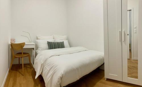 een witte slaapkamer met een bed en een bureau met een stoel bij Appartement confortable et complet in Clichy