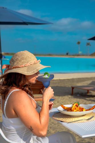a woman sitting at a table at the beach with a drink at Karibao Resort Town in Playas
