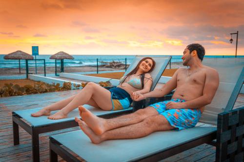 a man and woman sitting on a bench at the beach at Karibao Resort Town in Playas