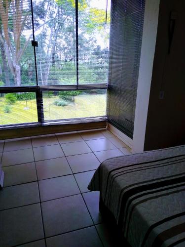 a bedroom with a bed and a window with a view at Apart Res Swiss - Jd Europa in Santa Cruz do Sul