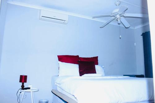 a white bed with red pillows and a ceiling fan at Sun & Night in Empangeni