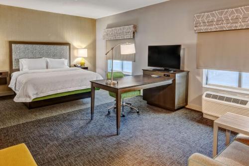 Habitación de hotel con cama y escritorio con TV. en Hampton Inn & Suites San Jose Airport en San José