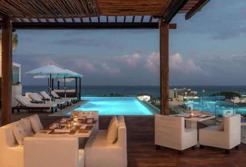 a resort with a pool and white chairs and a table at The Fives Downtown Hotel & Residences, Curio Collection by Hilton in Playa del Carmen