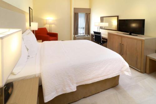 een hotelkamer met een wit bed en een televisie bij Hampton Inn Monterrey-Airport in Monterrey