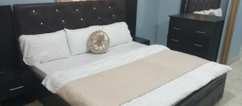 uma cama grande com uma cabeceira preta e almofadas brancas em De-Convenant Apartment em Abuja