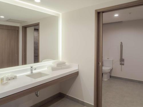 a bathroom with a sink and a mirror and a toilet at Hilton Garden Inn Santa Ana, San Jose in San José