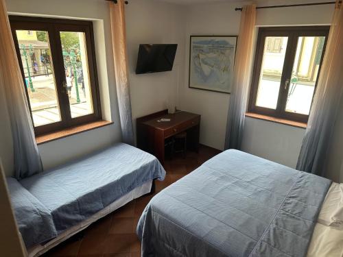 a bedroom with two beds and a desk and two windows at Hotel Alla città di Trieste in Grado