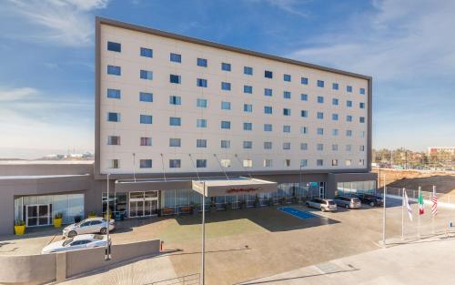 ein großes weißes Gebäude mit Autos auf einem Parkplatz in der Unterkunft Hampton Inn By Hilton Tijuana in Tijuana