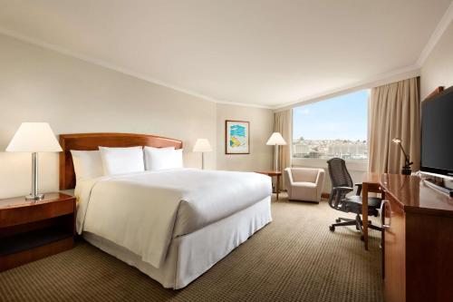 um quarto de hotel com uma grande cama branca e uma secretária em Hilton Colon Quito Hotel em Quito