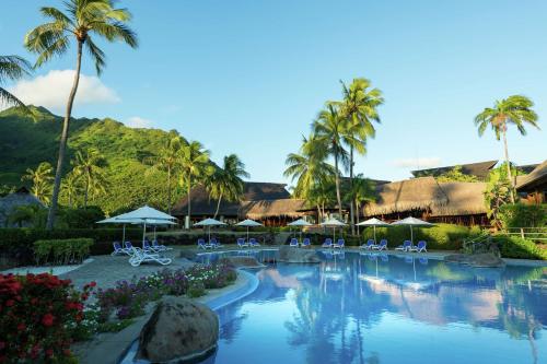 a swimming pool with chairs and umbrellas at a resort at Hilton Moorea Lagoon Resort & Spa in Papetoai