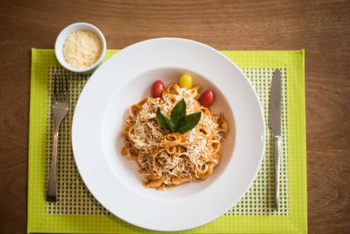 a white bowl of spaghetti with tomatoes and a green garnishment at Hampton By Hilton Santo Domingo Airport in Boca Chica