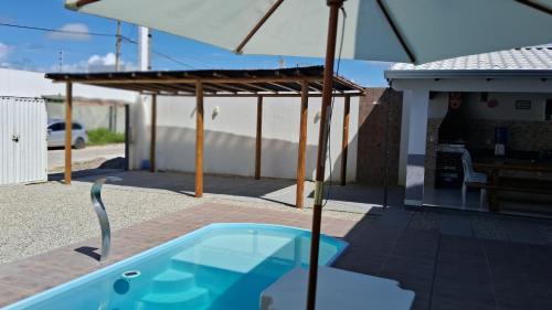 a swimming pool with an umbrella on a patio at Casa com piscina e espaço gourmet a 30m da praia! in Alcobaça