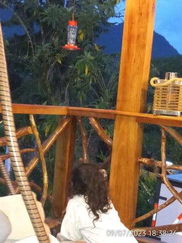 a woman sitting on the balcony of a tree house at El Guayabal de Mindo in Mindo