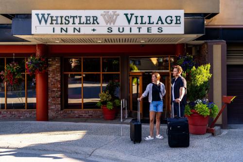 a man and a woman standing in front of a building with luggage at Whistler Village Inn & Suites in Whistler