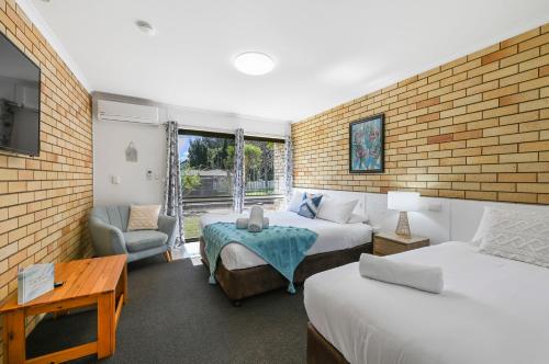 a bedroom with two beds and a chair and a table at Motel Glenworth in Toowoomba
